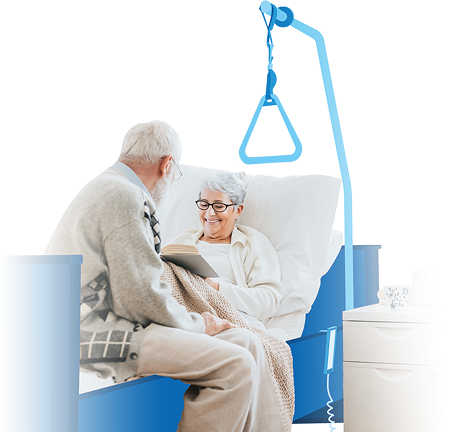 Couple de seniors complices, dont une femme alité lisant un livre dans un lit médicalisé SOS Oxygène équipé d'une potence d'aide au lever pour le maintien à domicile.